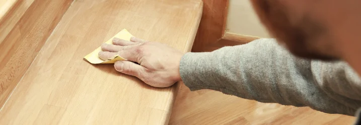 Person schleift mit Schleifpapier eine Treppenstufe aus Holz